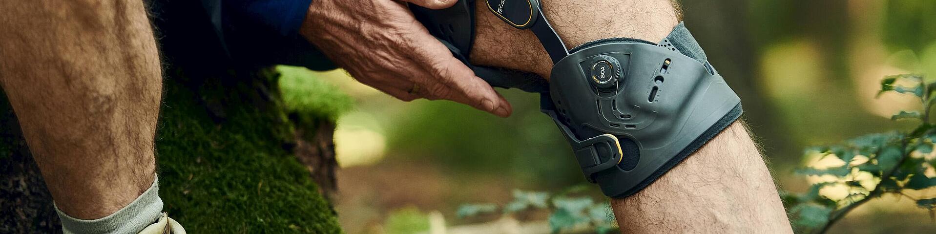 Knie-Orthese Unloader One X von Össur beim Sitzen auf einem Baumstumpf während einer Waldwanderung, © Copyrights by Össur hf