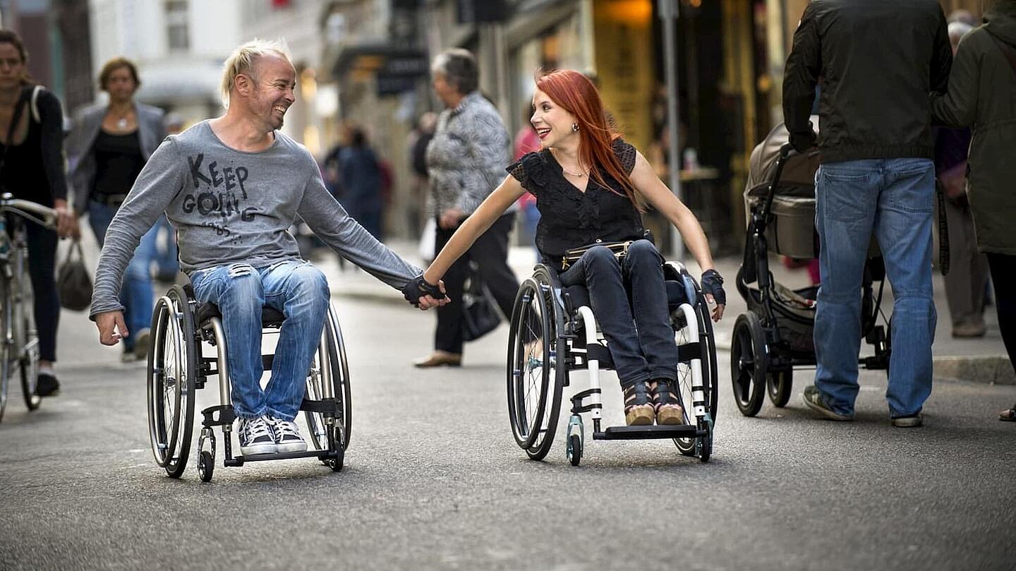 glückliches Paar aus Mann und Frau, die händehaltend im Rollstuhl sitzen, ©Invacare