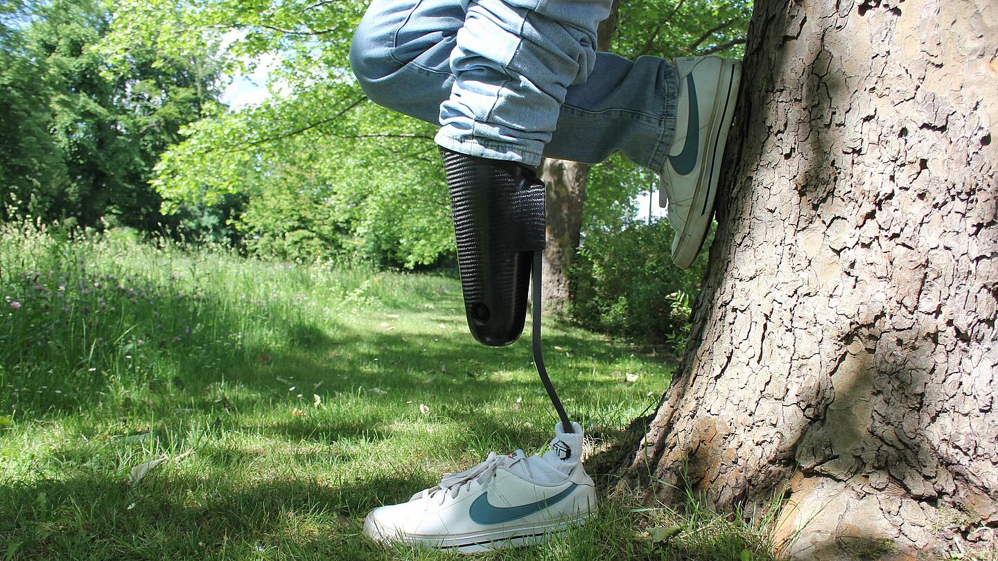 Träger einer Unterschenkel-Sportprothese mit Cheetah-Prothesenfuß lehnt am Baum