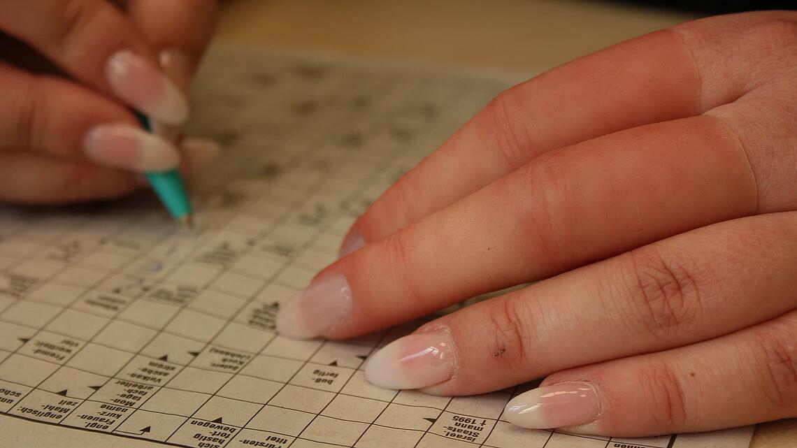 Hand mit zwei Fingerprothesen aus Silikon beim Ausfüllen eines Kreuzworträtsels